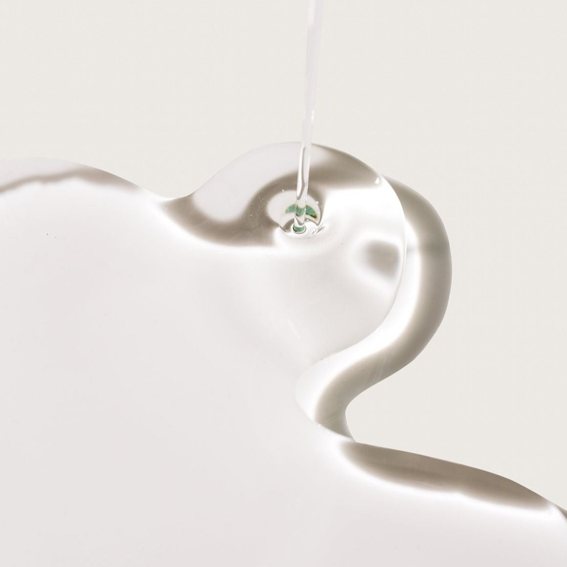 Close-up of Royal Hydrating Hair Oil texture, flowing from a 50ml bottle in an asymmetrical shape on a white surface, highlighting its rich, nourishing consistency for soft and shiny hair.