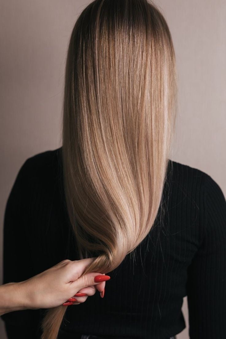 Back view of a woman with smooth, shiny blonde hair being gently held by a hand