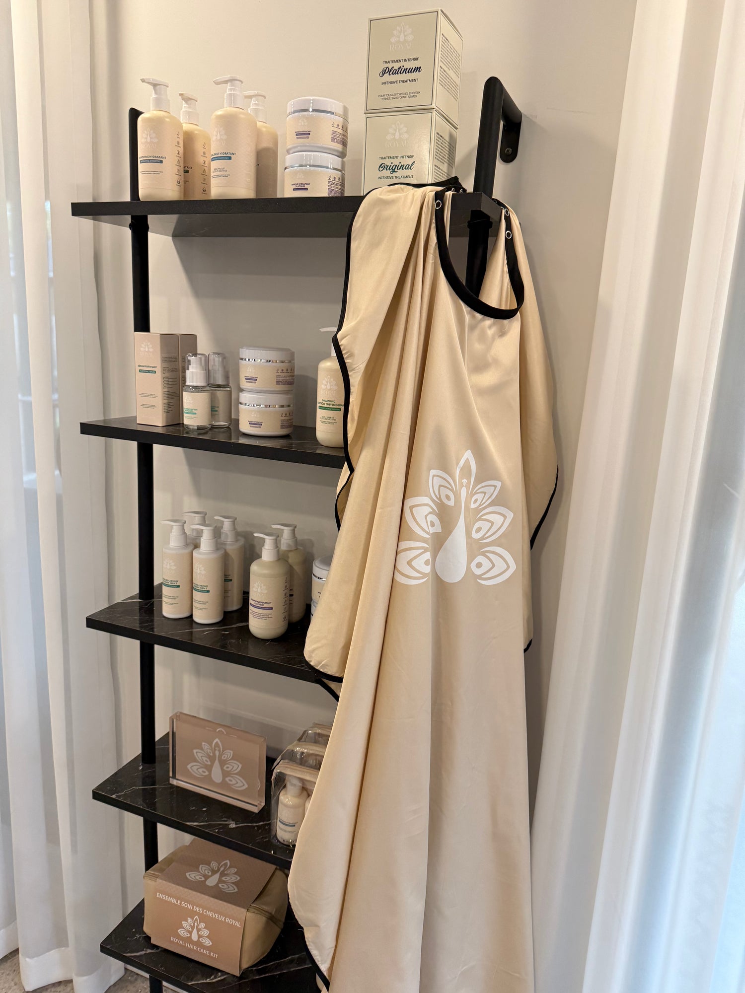ROYAL hair care products displayed on black shelves, with a beige branded salon apron hanging in front.